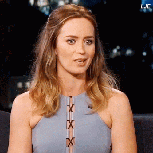A Woman In A Blue Dress Is Sitting In Front Of A Sign That Says Lje GIF
