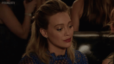 A Woman In A Blue Dress Is Sitting On A Couch In A Crowd Of People . GIF