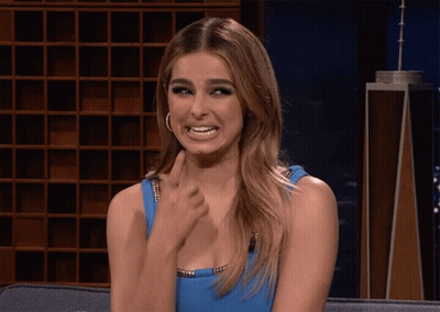 A Woman In A Blue Dress Is Sitting On A Couch Making A Funny Face GIF