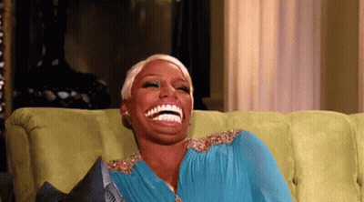 A Woman In A Blue Dress Is Sitting On A Green Couch And Laughing . GIF