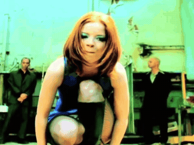 A Woman In A Blue Dress Is Squatting Down With A Man In A Suit Behind Her GIF