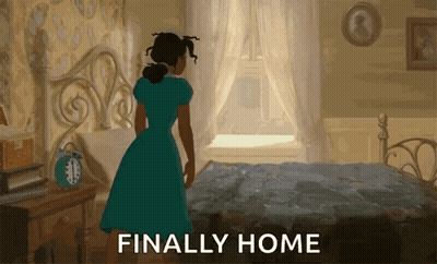 A Woman In A Blue Dress Is Standing In Front Of A Bed With The Words Finally Home Written Below Her GIF