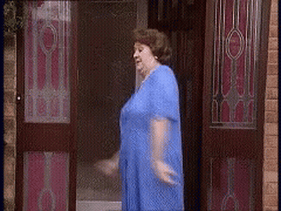 A Woman In A Blue Dress Is Standing In Front Of A Door GIF