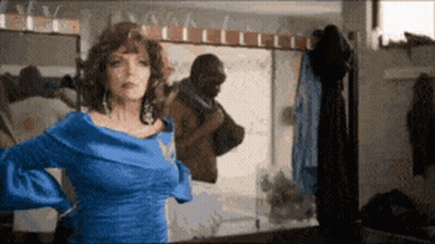 A Woman In A Blue Dress Is Standing In Front Of A Mirror Looking At Herself GIF