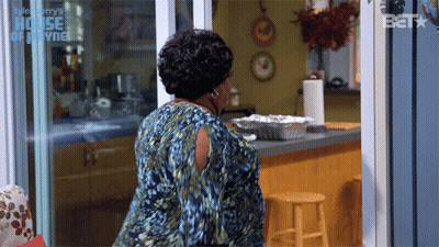 A Woman In A Blue Dress Is Standing In Front Of A Sliding Glass Door That Says House Of Payne GIF