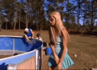 A Woman In A Blue Dress Is Standing In Front Of A Swimming Pool GIF