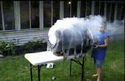 A Woman In A Blue Dress Is Standing In Front Of A Table With Smoke Coming Out Of It GIF