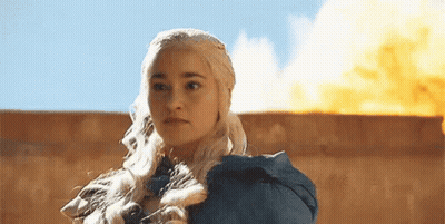 A Woman In A Blue Dress Is Standing In Front Of A Wall With A Fire In The Background . GIF