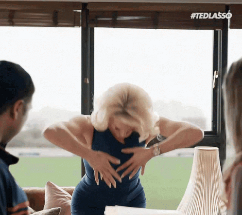 A Woman In A Blue Dress Is Standing In Front Of A Window With Her Hands On Her Hips . GIF