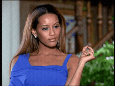 A Woman In A Blue Dress Is Standing In Front Of A Wooden Staircase GIF