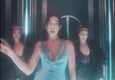 A Woman In A Blue Dress Is Standing In Front Of Three Dancers In A Dark Room . GIF