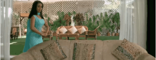 A Woman In A Blue Dress Is Standing Next To A Couch In A Living Room GIF