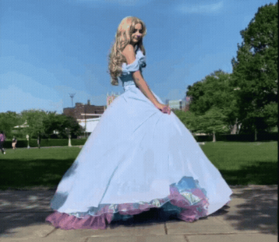 A Woman In A Blue Dress Is Standing On A Sidewalk GIF