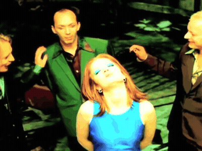 A Woman In A Blue Dress Is Surrounded By Men In Green Suits . GIF