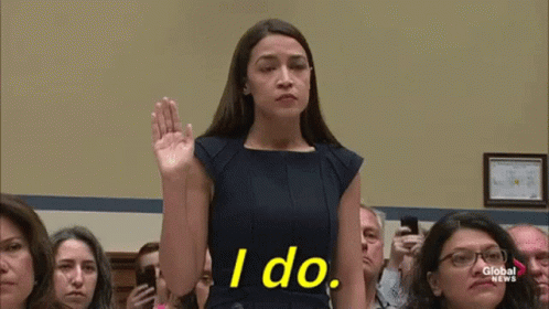 A Woman In A Blue Dress Is Taking A Oath In Front Of A Crowd Of People . GIF