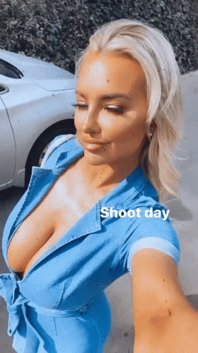 A Woman In A Blue Dress Is Taking A Selfie In Front Of A White Car GIF