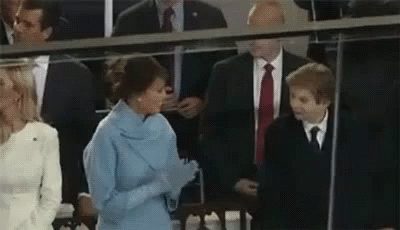 A Woman In A Blue Dress Is Talking To A Young Boy In A Suit And Tie . GIF