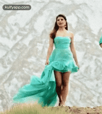 A Woman In A Blue Dress Is Walking Across A Hill . GIF