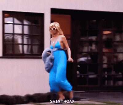 A Woman In A Blue Dress Is Walking In Front Of A Building With Sainthoax Written On The Bottom GIF
