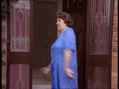 A Woman In A Blue Dress Is Walking Through A Door GIF