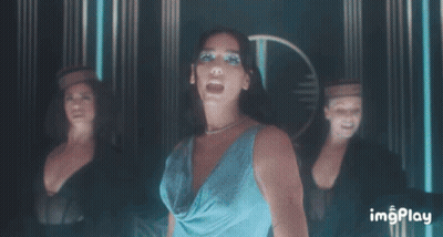 A Woman In A Blue Dress Stands In Front Of A Group Of Dancers With Imgplay Written On The Bottom Right GIF