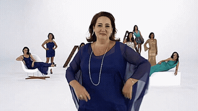 A Woman In A Blue Dress Stands In Front Of A Group Of Women In Different Dresses GIF