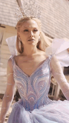 A Woman In A Blue Dress With A Crown On Her Head Is Standing In Front Of A Building . GIF