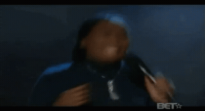 A Woman In A Blue Head Scarf Is Dancing In A Dark Room While Holding A Racket . GIF