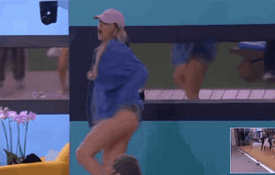 A Woman In A Blue Jacket And Pink Hat Is Dancing In Front Of A Window GIF
