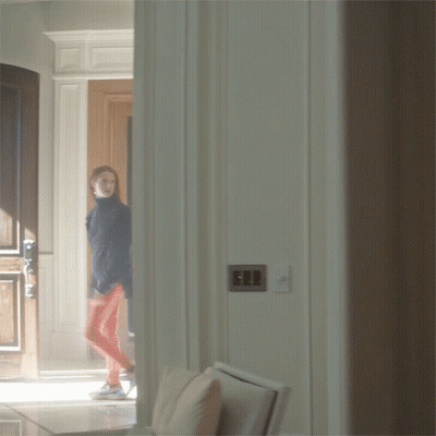 A Woman In A Blue Jacket And Red Pants Is Walking Through A Doorway GIF