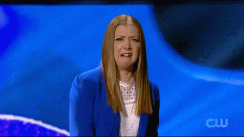 A Woman In A Blue Jacket And White Shirt Is Making A Funny Face On A Blue Background . GIF