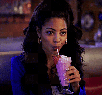A Woman In A Blue Jacket Is Drinking A Pink Milkshake With Whipped Cream And Strawberries . GIF