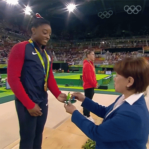 A Woman In A Blue Jacket Is Giving A Medal To Another Woman GIF
