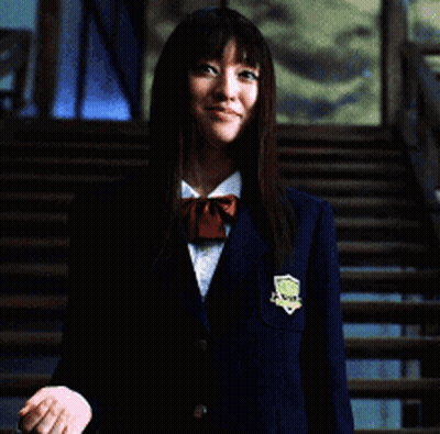 A Woman In A Blue Jacket Is Holding A Chain Around Her Neck And Smiling GIF