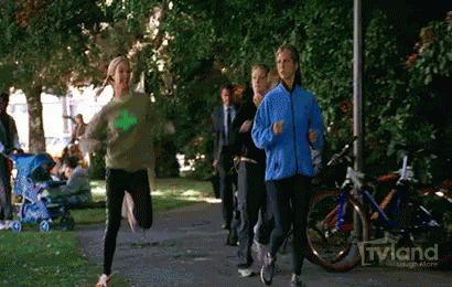 A Woman In A Blue Jacket Is Running In A Park With A Tvland Logo In The Background GIF