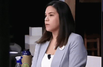 A Woman In A Blue Jacket Is Sitting At A Table With A Microphone On Her Head . GIF