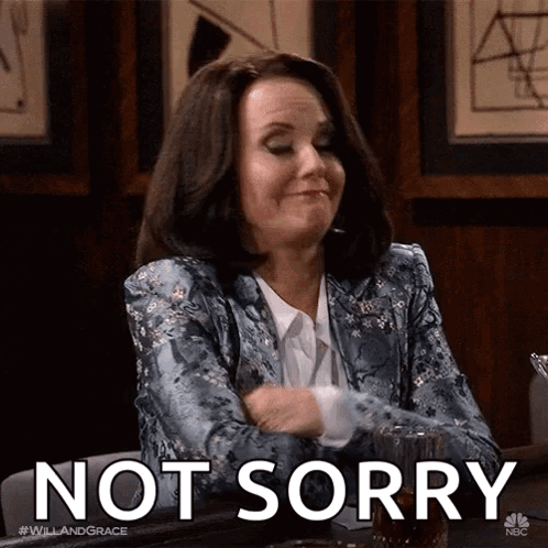 A Woman In A Blue Jacket Is Sitting At A Table With Her Arms Crossed And Says Not Sorry GIF