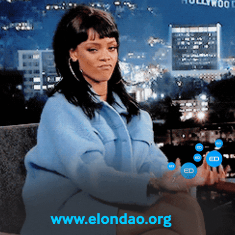 A Woman In A Blue Jacket Is Sitting In Front Of A Sign That Says Hollywood GIF