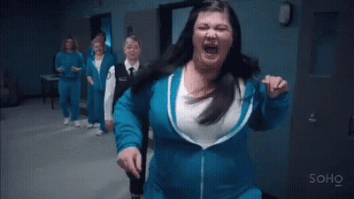 A Woman In A Blue Jacket Is Standing In A Hallway With A Group Of Women . GIF