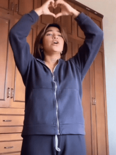A Woman In A Blue Jacket Making A Heart With Her Hands GIF