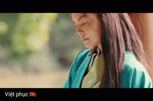 A Woman In A Blue Jacket Stands In Front Of A Sign That Says Viet Phuc GIF