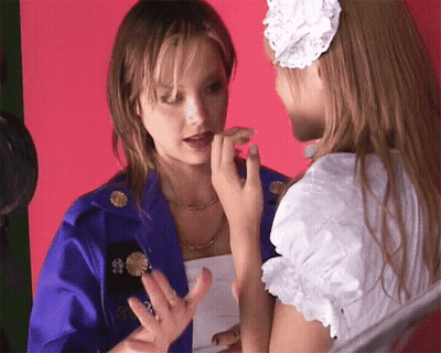 A Woman In A Blue Jacket With Chinese Writing On It Is Talking To Another Woman In A White Dress GIF