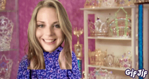 A Woman In A Blue Leopard Print Shirt Is Smiling In Front Of A Shelf Full Of Tiaras And The Words Gif Jif GIF