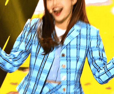 A Woman In A Blue Plaid Jacket Is Dancing On A Yellow Background GIF