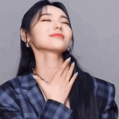 A Woman In A Blue Plaid Jacket Is Holding Her Hand To Her Chest . GIF