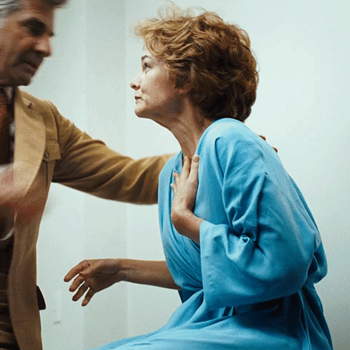 A Woman In A Blue Robe Is Being Held By A Man In A Tan Suit GIF