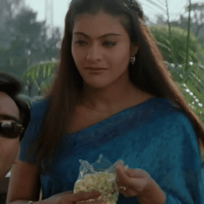A Woman In A Blue Saree Is Holding A Bag Of Popcorn . GIF