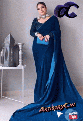 A Woman In A Blue Saree Is Standing In Front Of A White Table GIF