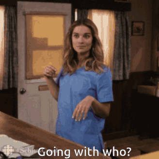 A Woman In A Blue Scrub Top Is Standing In Front Of A Door With The Words " Going With Who " Written Below Her GIF