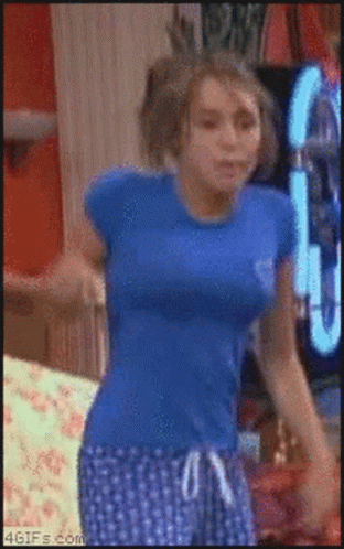 A Woman In A Blue Shirt And Blue Polka Dot Shorts Is Dancing In A Room GIF